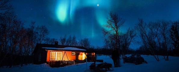 En opplyst hytte i vinterlandskap med nordlys over himmelen